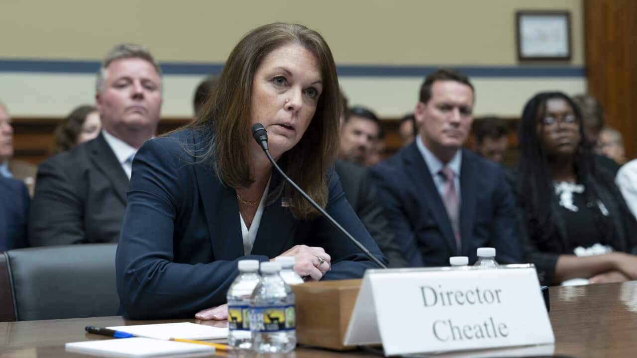 A woman in a blue suit sits in front of a microphone at a hearing.