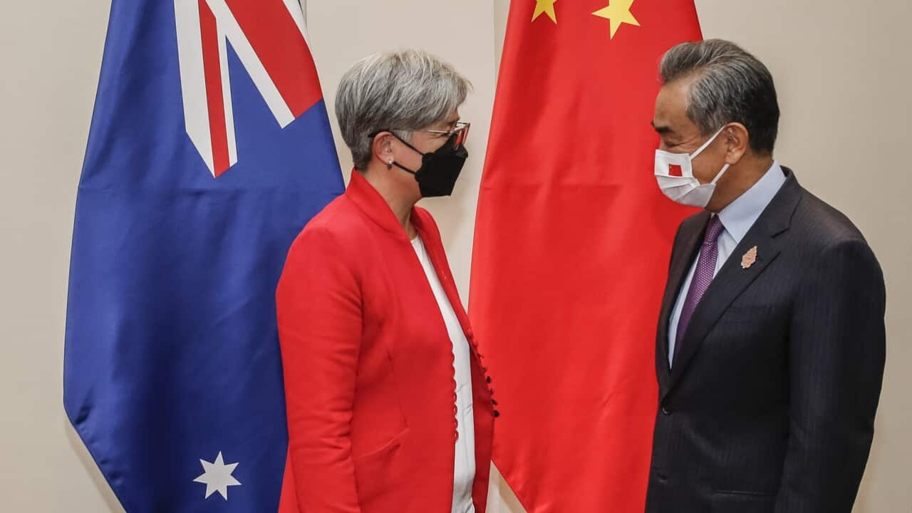Side profiles of Penny Wong and Wang Yi standing in front of Australia and China flags.