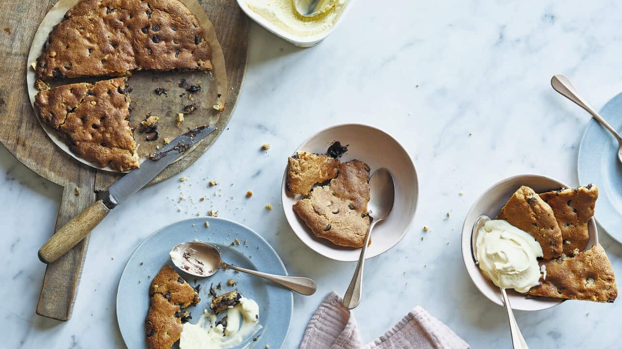 Blue plates and white bowls, holding wedges of choc-chip cookie and vanilla ice-cream, sit on a mable surface.
