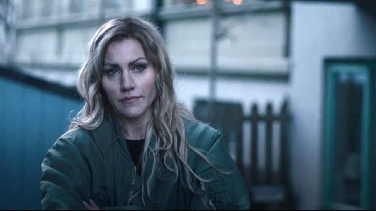 A woman with long blonde hair and a heavy jacket looks pensively forward