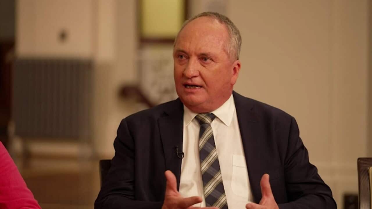 A man in a suit and tie talking in a beige room.