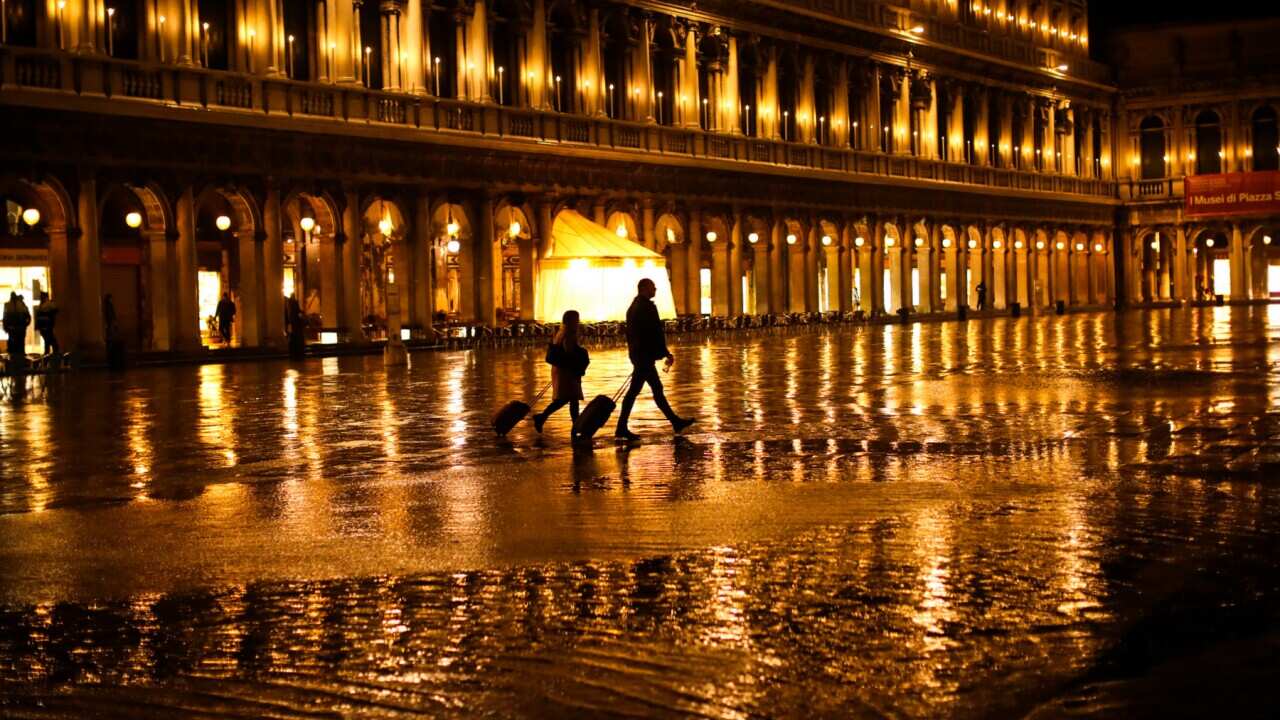 Tourists walk through a nearly empty St. Mark's Square on a rainy day in Venice