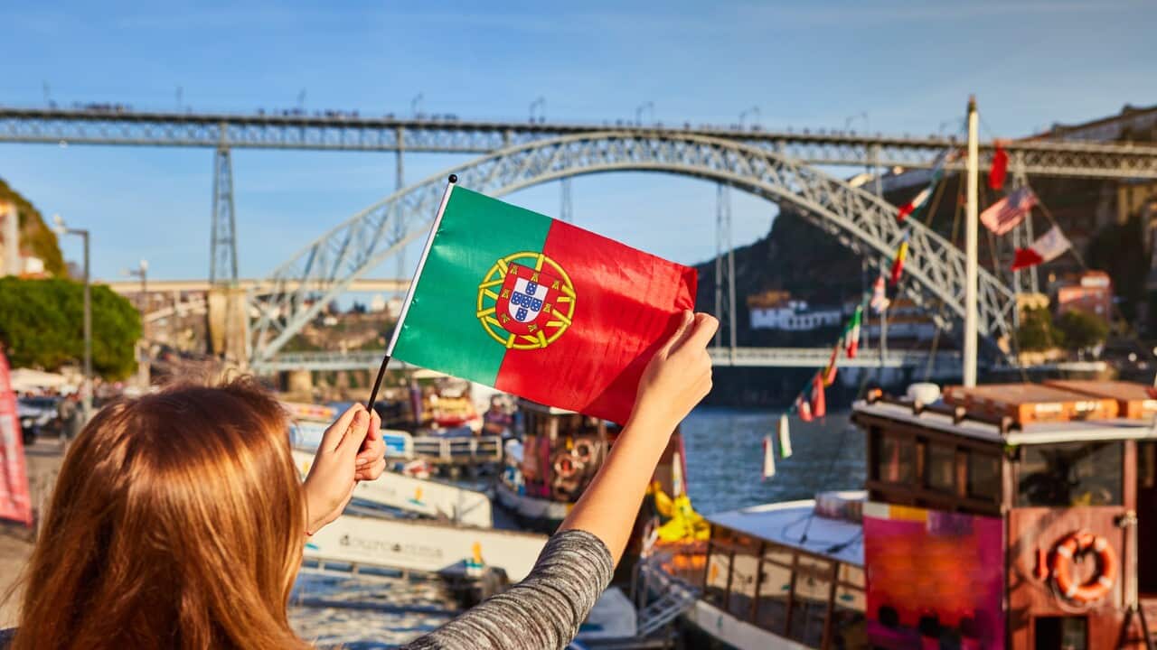 Young woman traveler standing back with portuguese flag, enjoying beautiful cityscape view on Douro river, bridge and boats during the morning light in Porto, Portugal