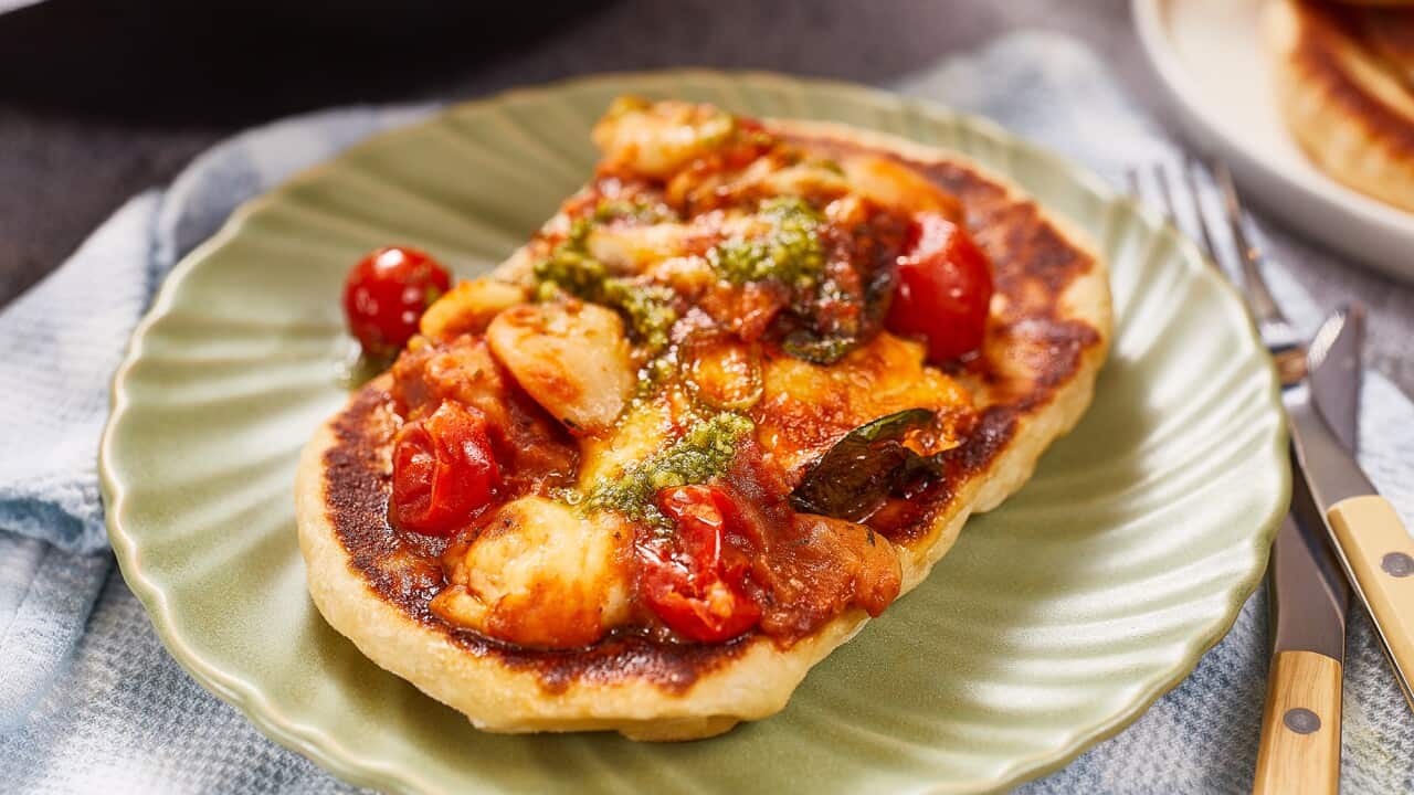 An oval-ish small flatbread is topped with a bean and tomato mix, topped with drizzles of pesto.