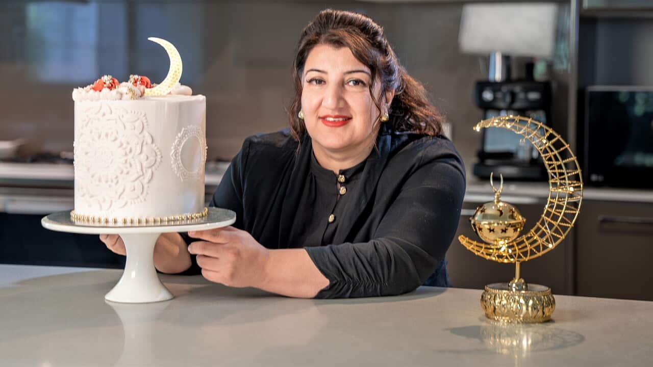 A woman with long bronw hair leans on a bench next to a white cake.
