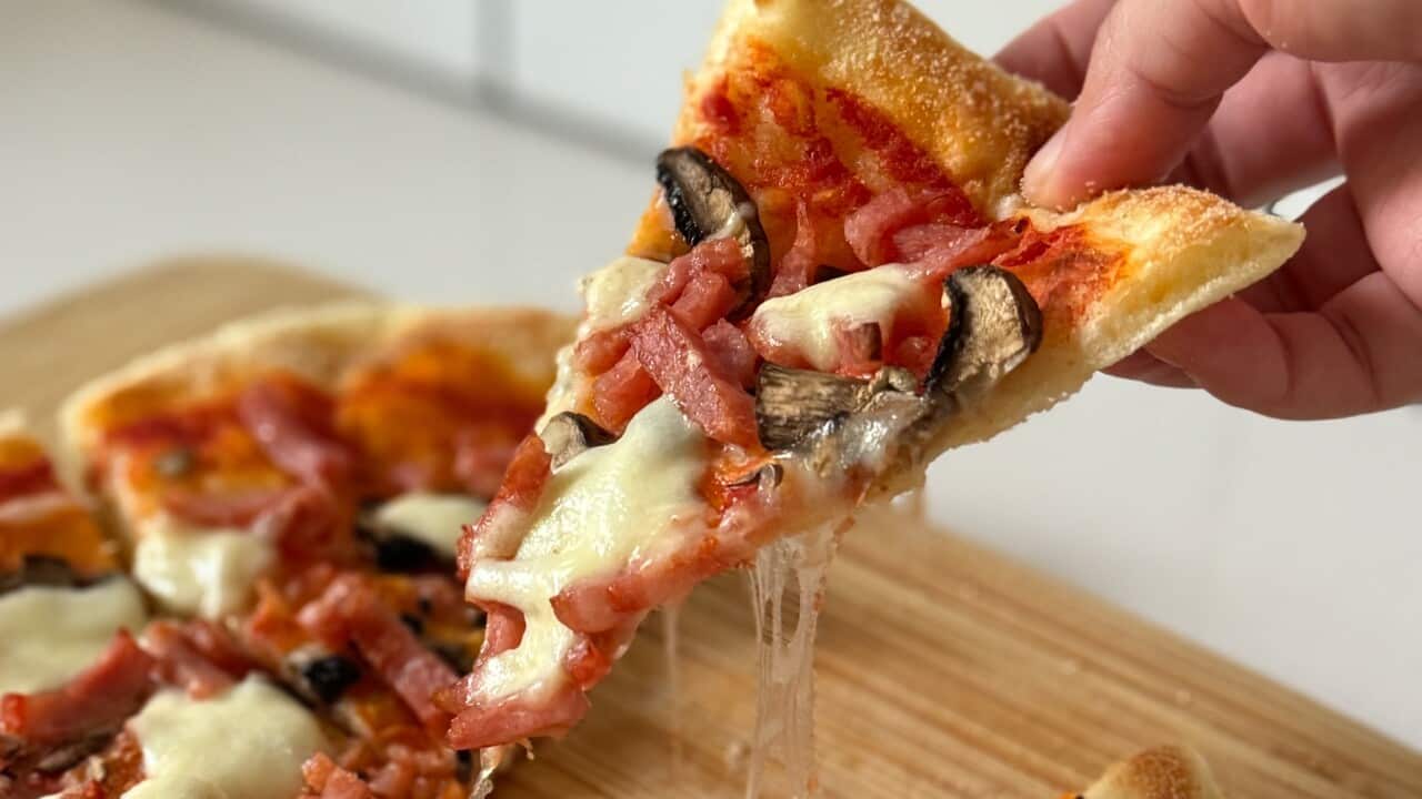 A slice of pizza getting pulled from the whole, with a webbing of cheese stretching from the slice.