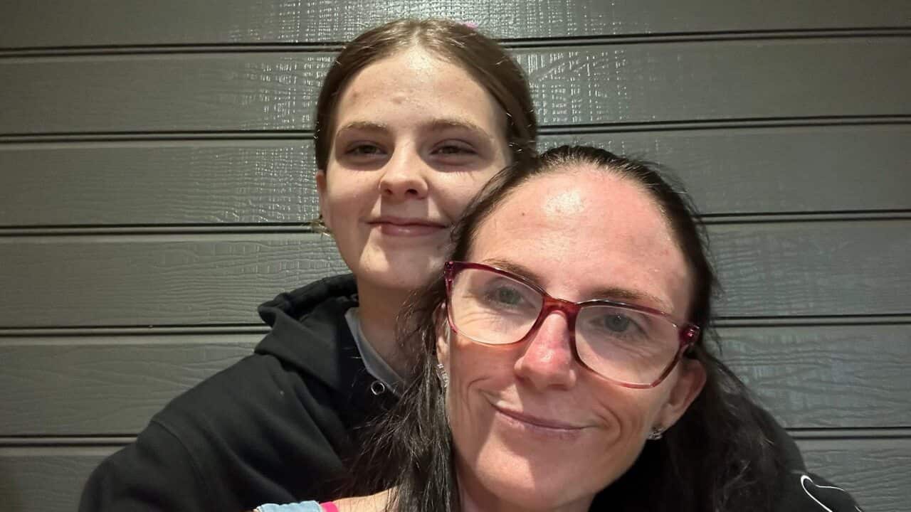 A woman wearing glasses is being hugged by a teenage girl.