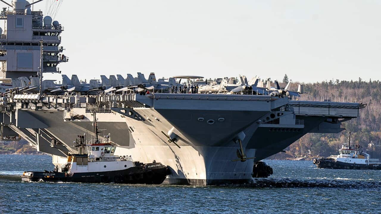 A large aircraft carrier on the sea, with two much smaller boats nearby.