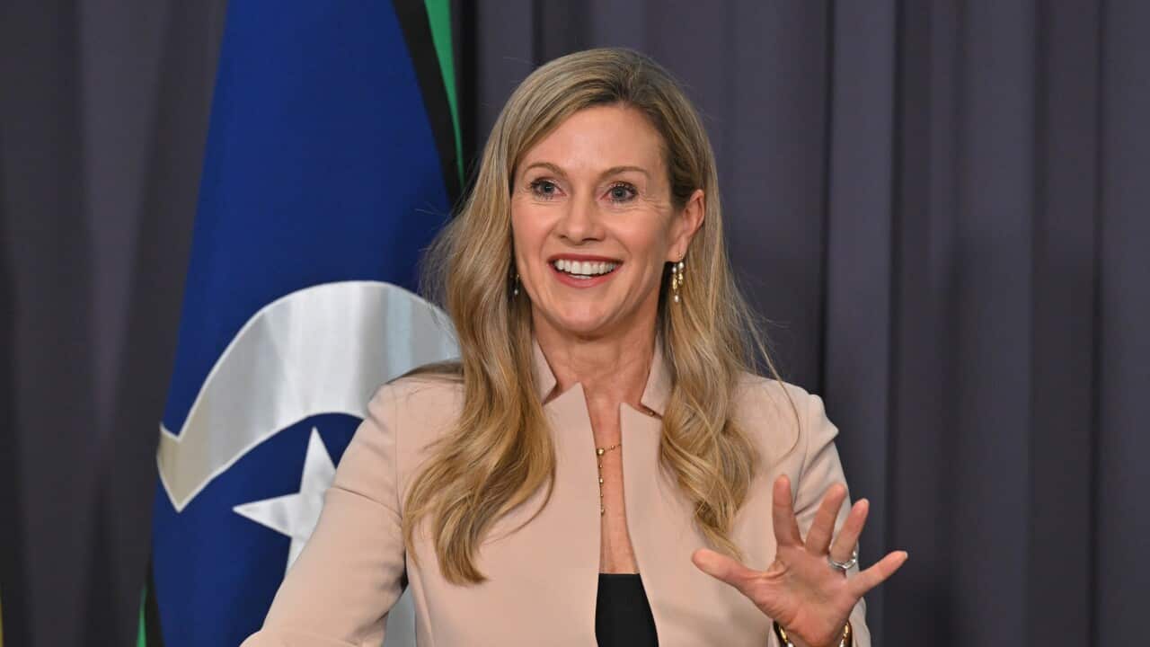 A woman with blonde hair in a tan jacket.