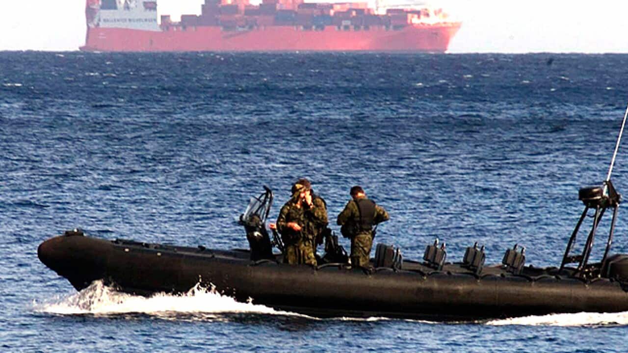 An Australian navy boat travels across the water with a large container ship in the background.