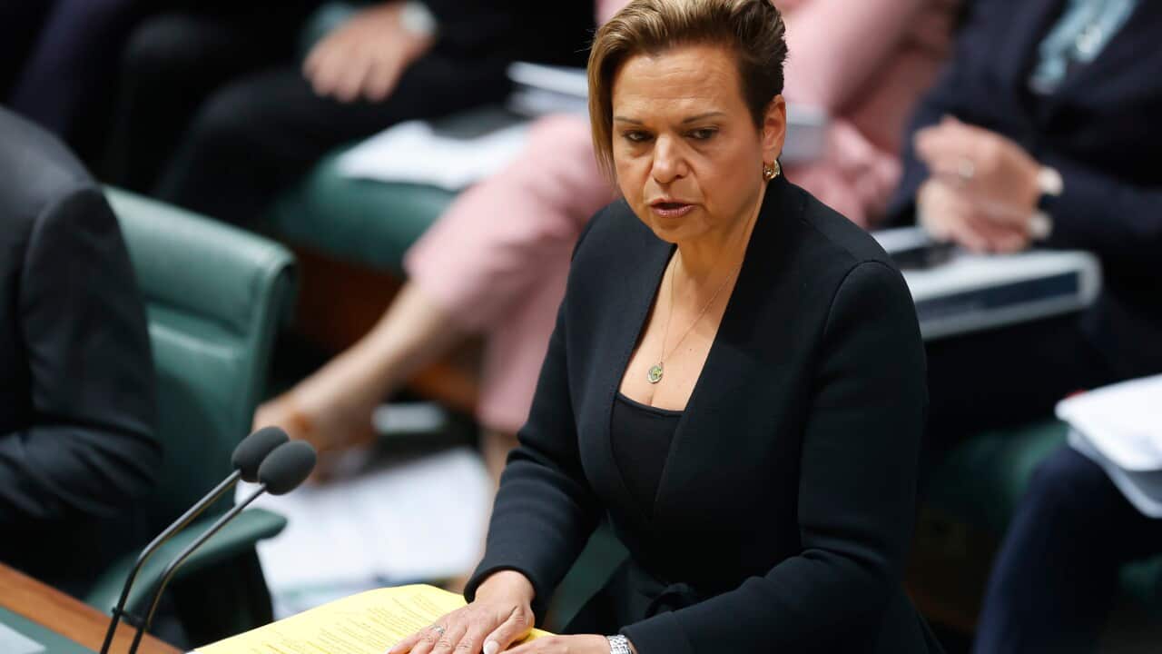 A woman in a black blazer speaks into a microphone.