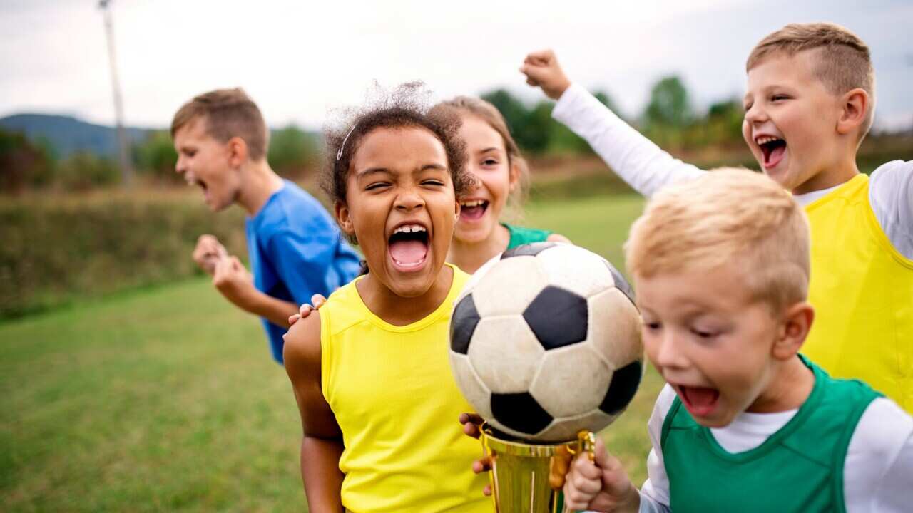 A group of children with cup prize standing outdoors on football pitch.