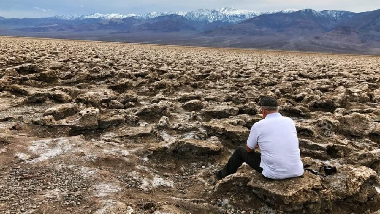 Rear View Of Man Sitting On Rock Against Mountains At Death Valley National Park