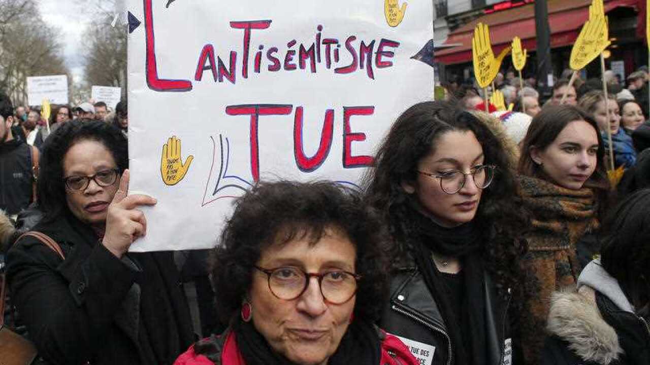 A woman in Paris holds a poster reading : "the anti-semitism kills"