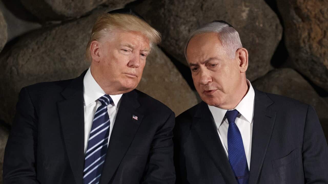 Two men in dark suits lean towards each other.