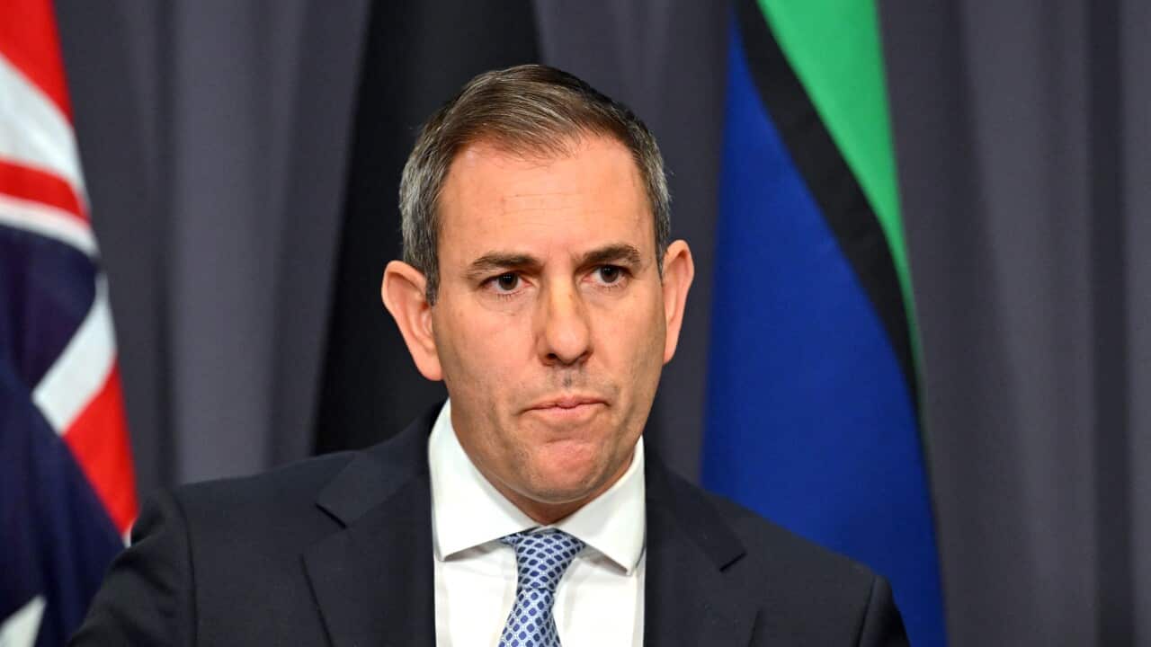 Jim Chalmers wearing a suit speaking at a podium with Australian, Aboriginal and Torres Strait Island flags in the background