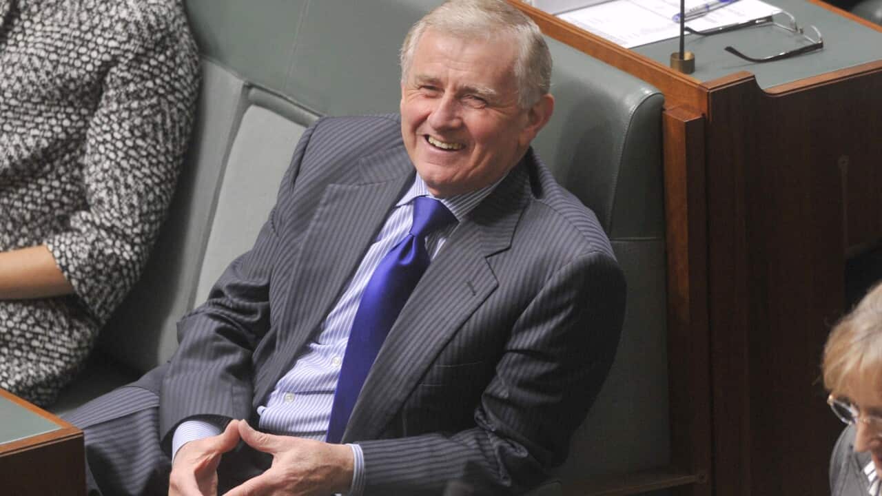 A man in a suit and tie sits and smiles.