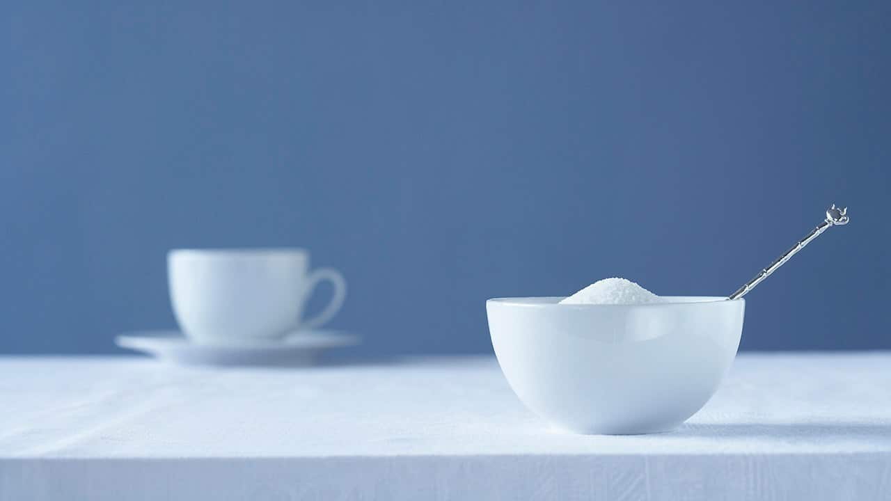 Bowl of sugar on table tea cup in background