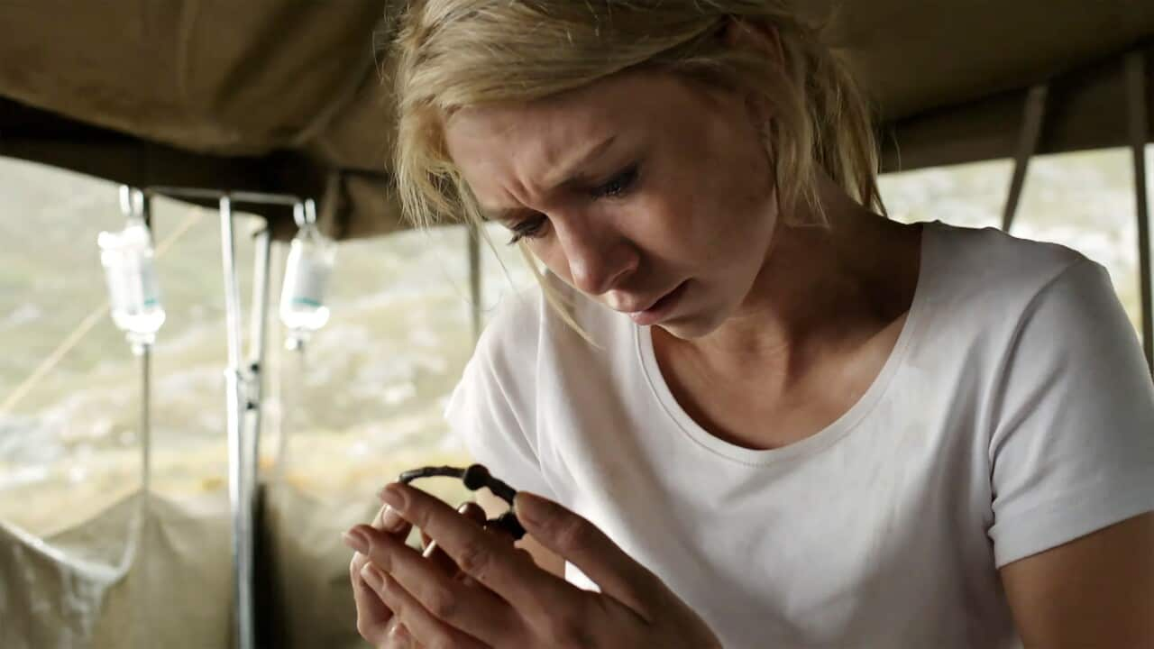 A women in a white shirt leans over what looks like a very old piece of jewellery. 