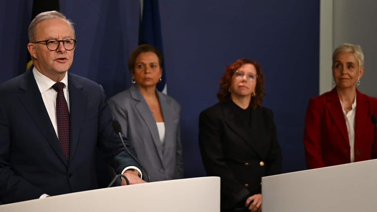A man and three women standing on a podium during a press conference