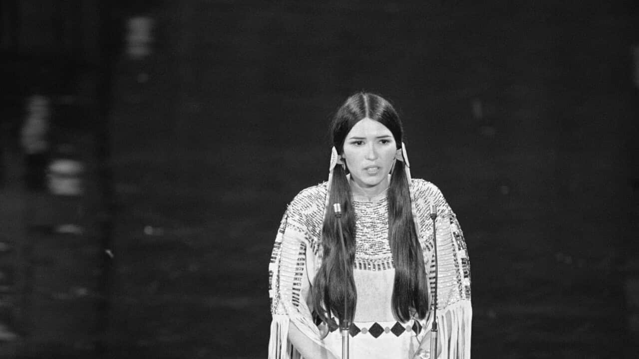 A woman in traditional Native American dress speaking at a podium