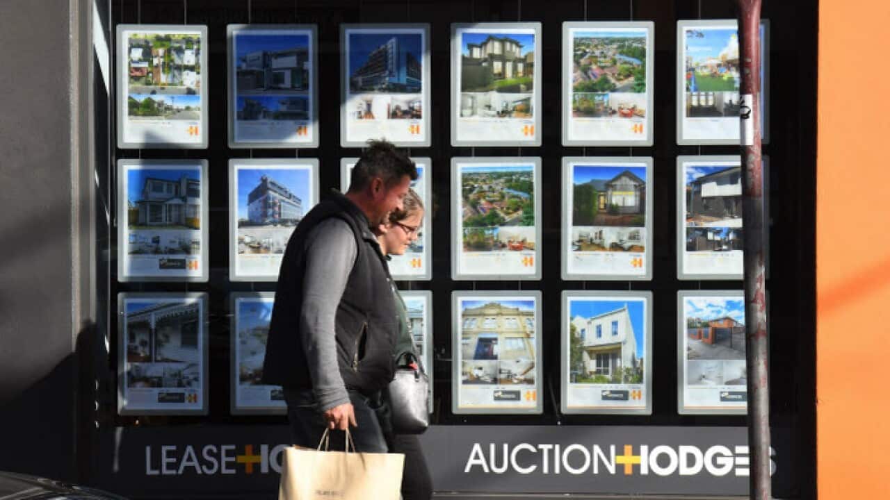 A couple walks past a real estate agent's window advertising houses for sale and auction in Melbourne