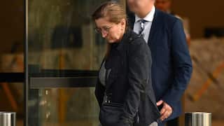 A mddle aged white woman wearing a dark suit jacket and glasses with her head down as she leaves a court house