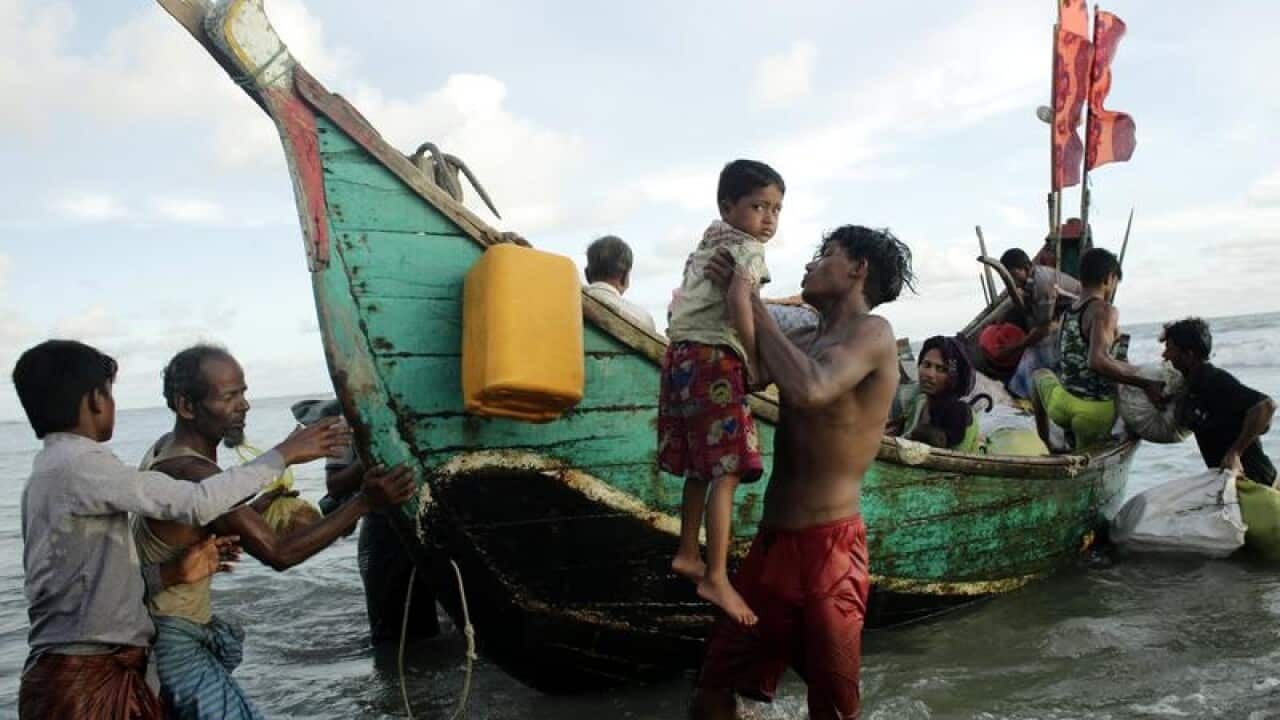 A Rohingya man helps a boy to disembark from a boat