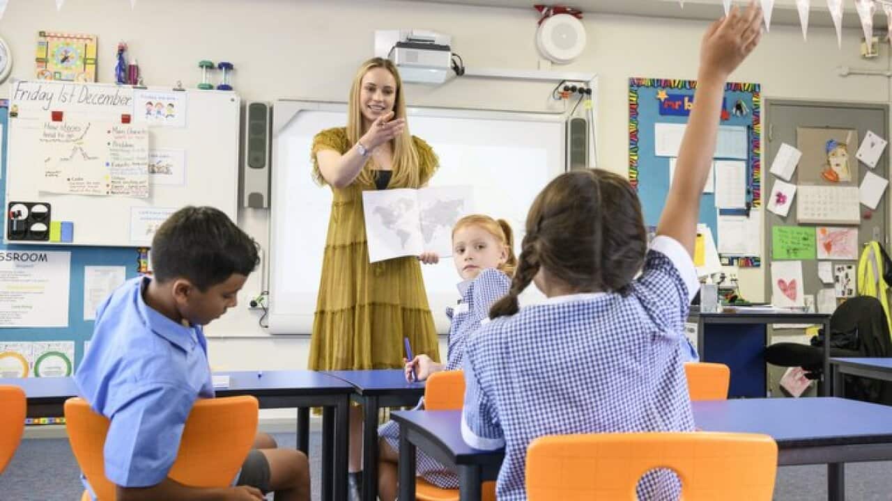 Young primary school teacher pointing at girl with arm raised in classroom