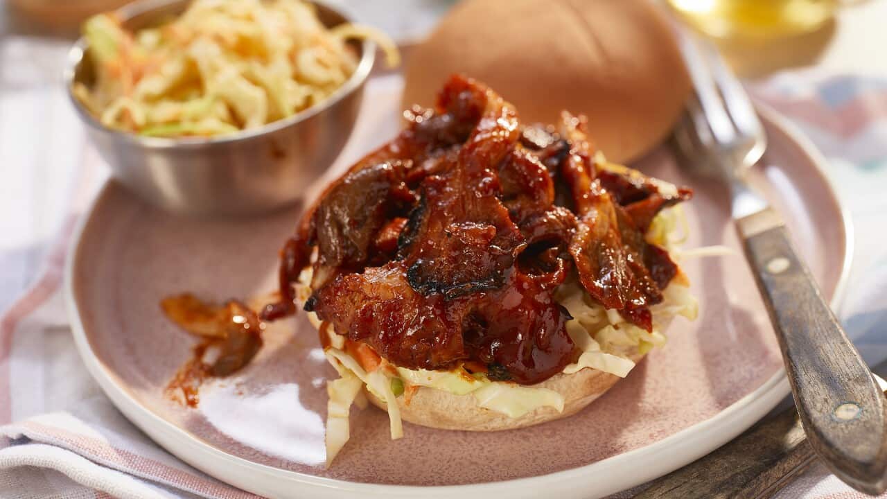 A burger bottom is topped with a little coleslaw and a mound of juicy, sticky mushroom pieces. The burger top sits alongside. More buns and coleslaw can be seen in the background.