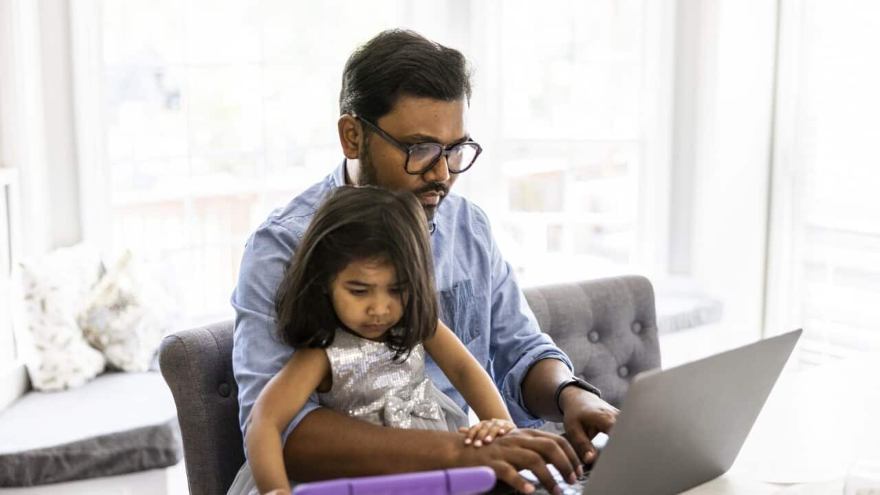 Father using laptop and smartphone while holding toddler daughter