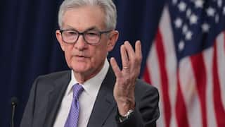 A man in a suit raises his hand as he speaks at a lectern