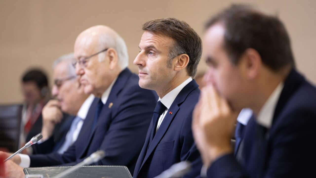 Several men, all wearing dark suits, sit in a row at what appears to be a diplomatic conference.