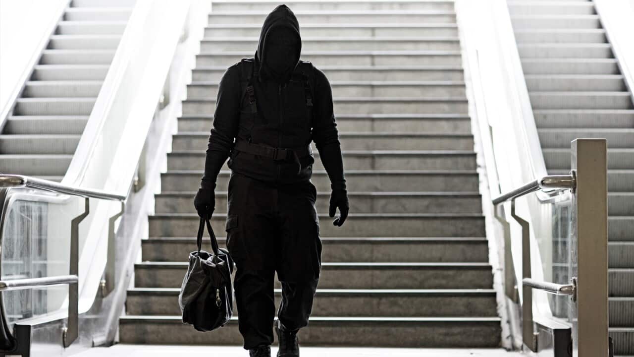 Hooded Lone wolf Man wearing black carrying bag in urban underground public transport setting