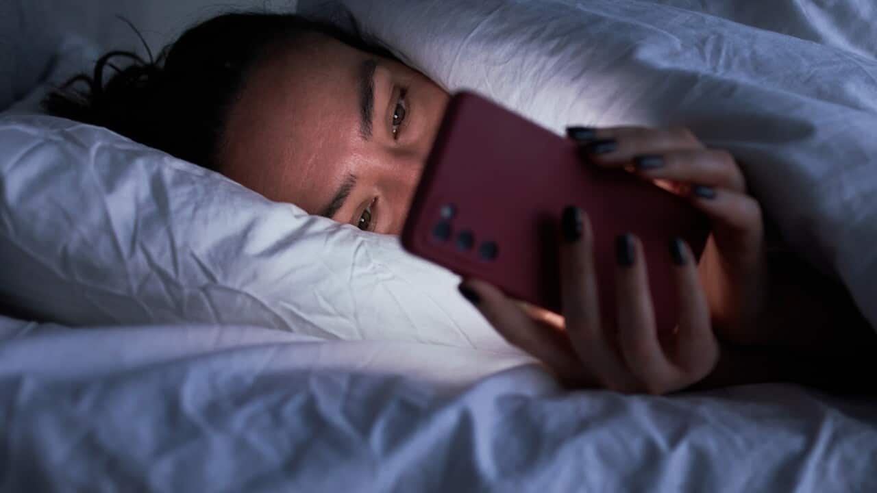 A woman is using her phone as she lies in bed.