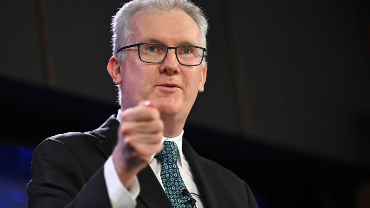A man with white hair in a suit and blue tie holding up his hand in a fist.