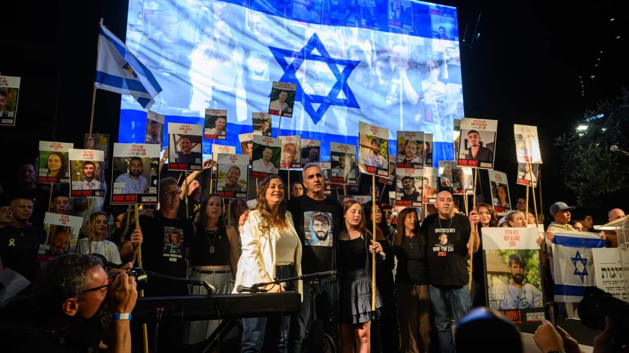 A group of people on a stage holding placards with pictures of the hostages taken by Hamas. A large Israeli flag is displayed on a screen behind them.
