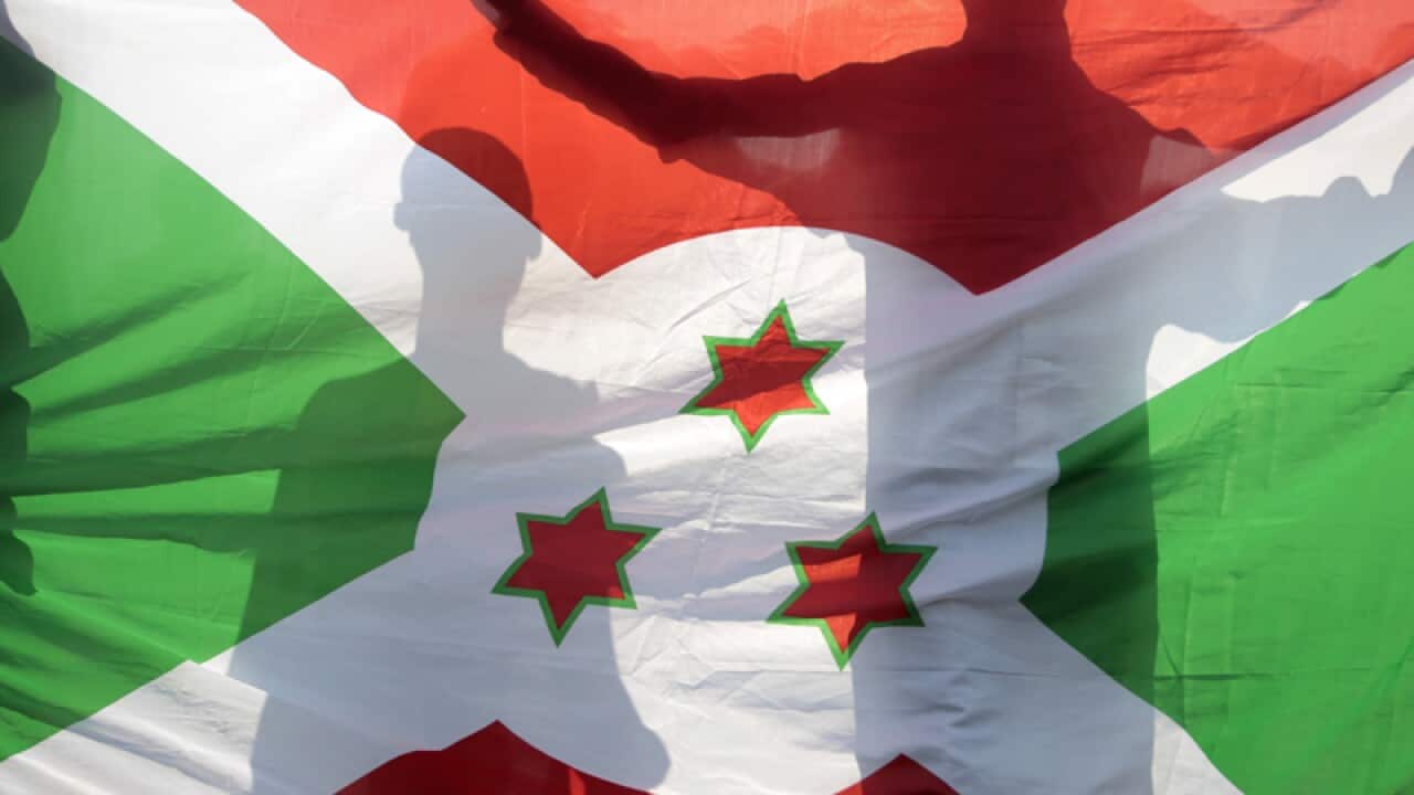 Mourners are silhouetted behind the Burundi national flag