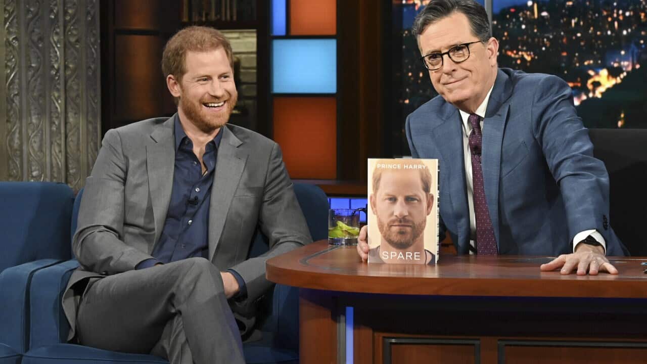 Prince Harry sitting on a chair next to talk show host Stephen Colbert, who is sitting at a desk.