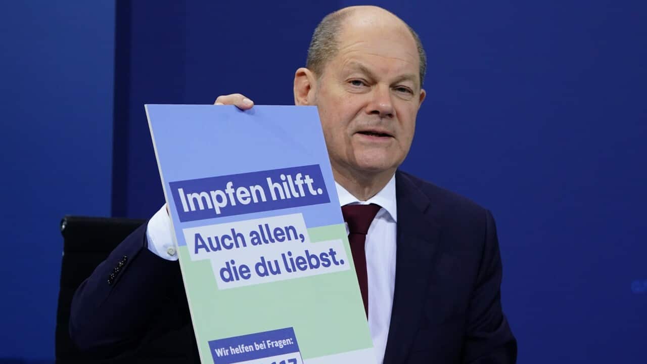 German Chancellor Olaf Scholz and sign saying 'vaccination helps'
