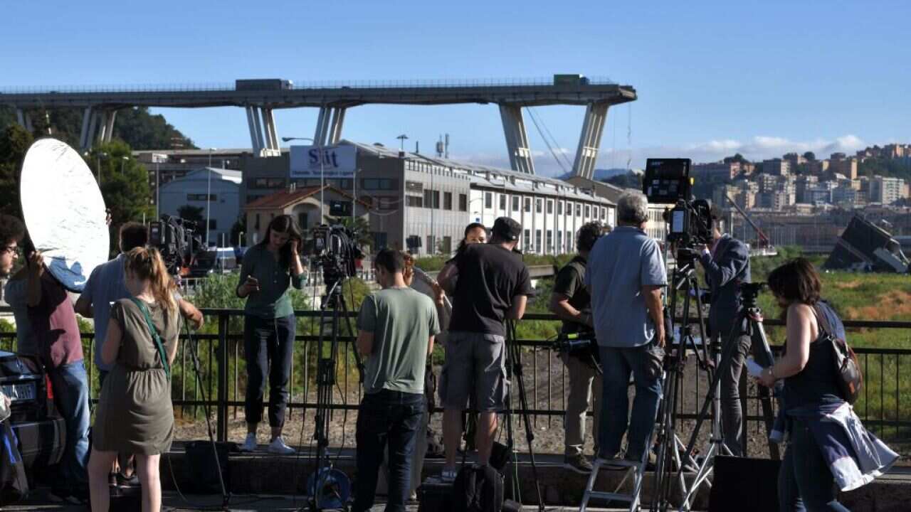 Media representatives work close to the Morandi motorway bridge after a section collapsed in the north-western Italian city of Genoa on August 15, 2018.