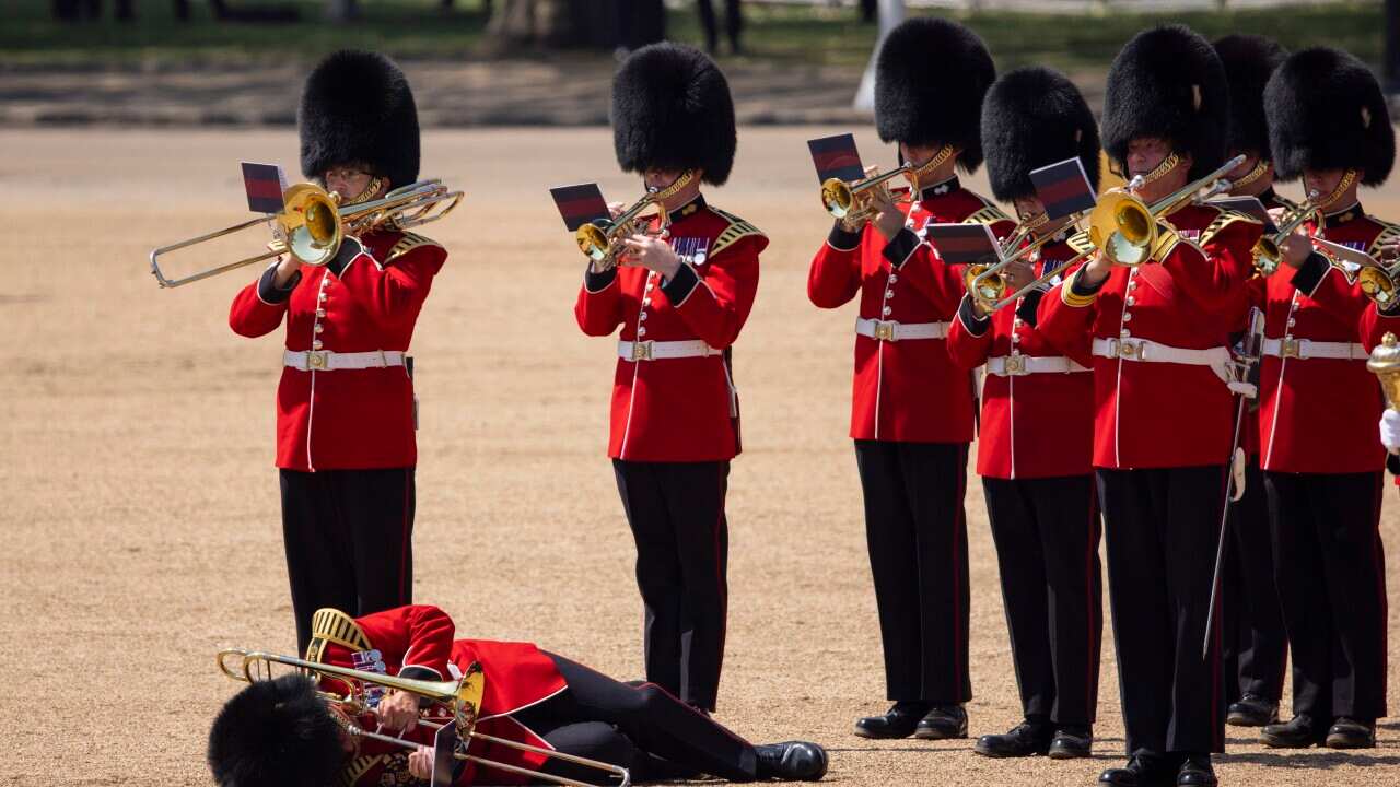 A soldier holding a trombone on the ground as others with musical instruments stand and play.