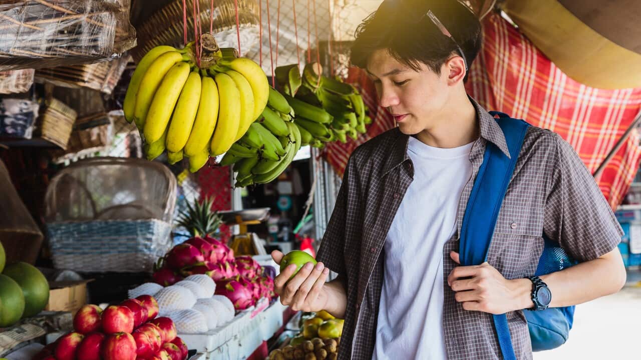 Young Asian traveller man enjoying selling fruites at traditional street market, Khonkaen city, Thailand