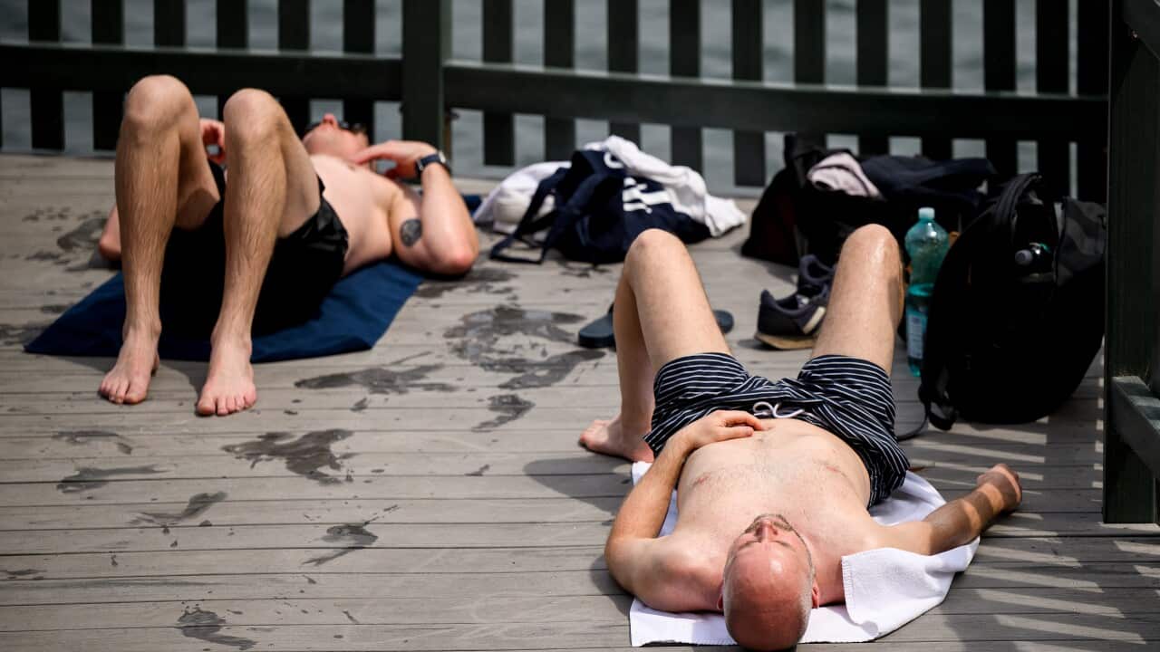 Two men lie on a wooden deck next to water
