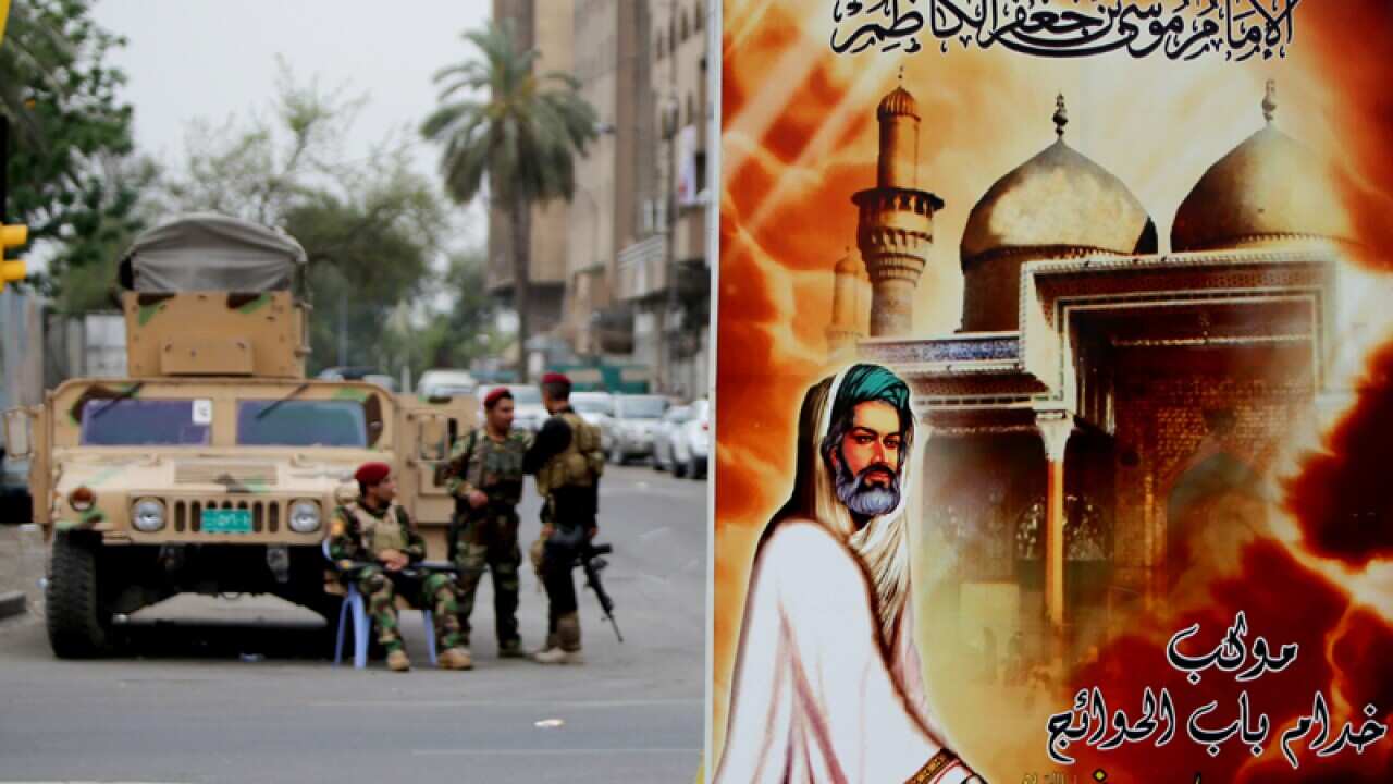 Iraqi security forces stand guard near a poster of a Shi'ite shrine