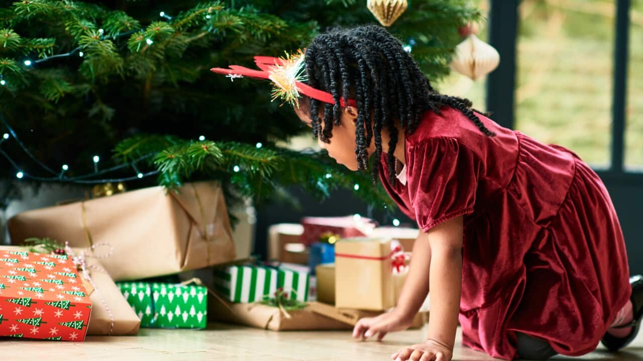 Young girl wearing red dress kneeling before Christmas presents under the tree