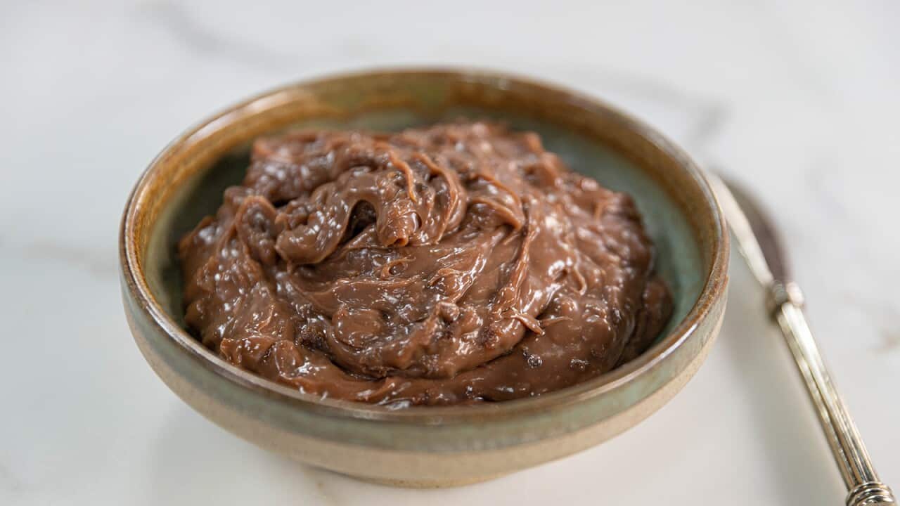 A green and cream round bowl is filled with a rich chocolate-coloured spread.