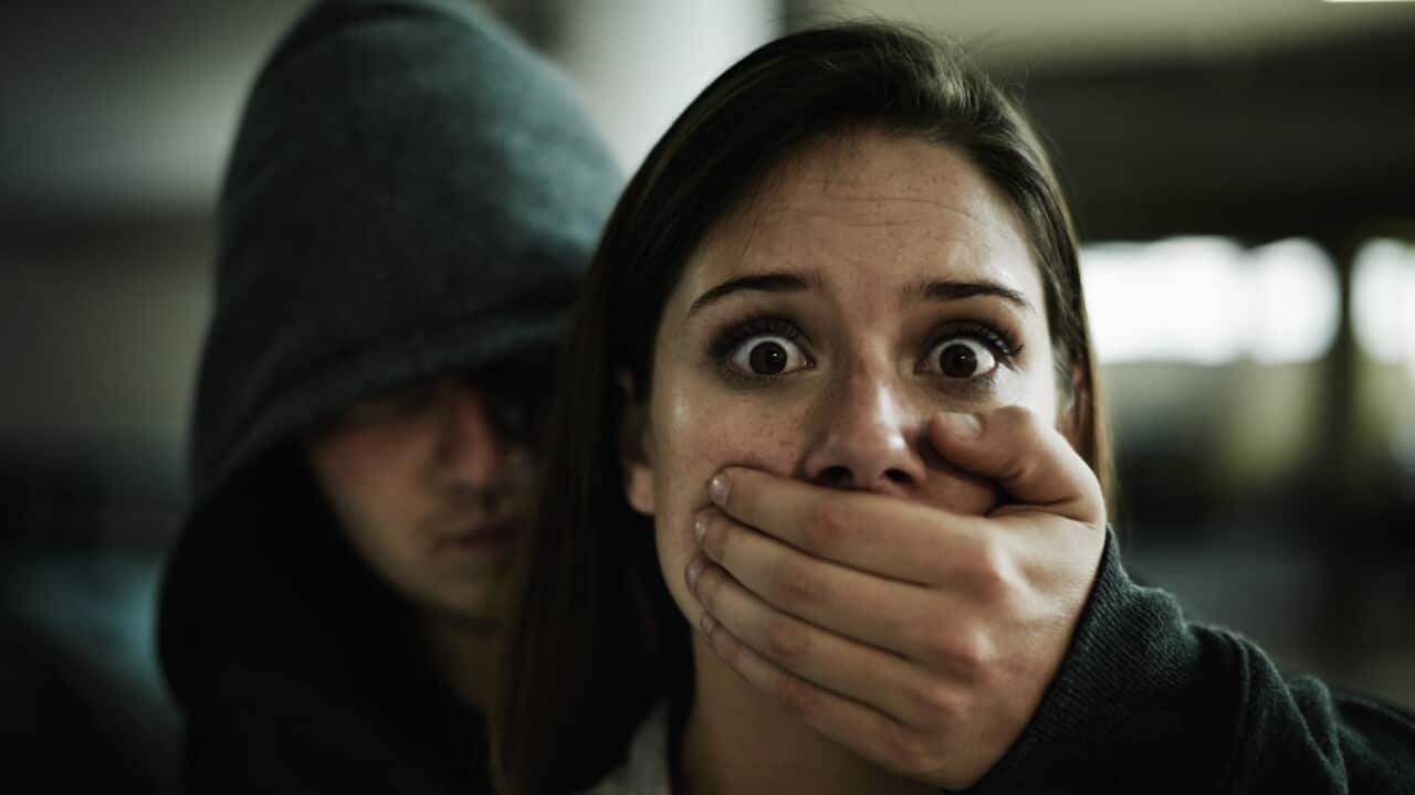 A terrified young woman held captive by a man with his hand over her mout
