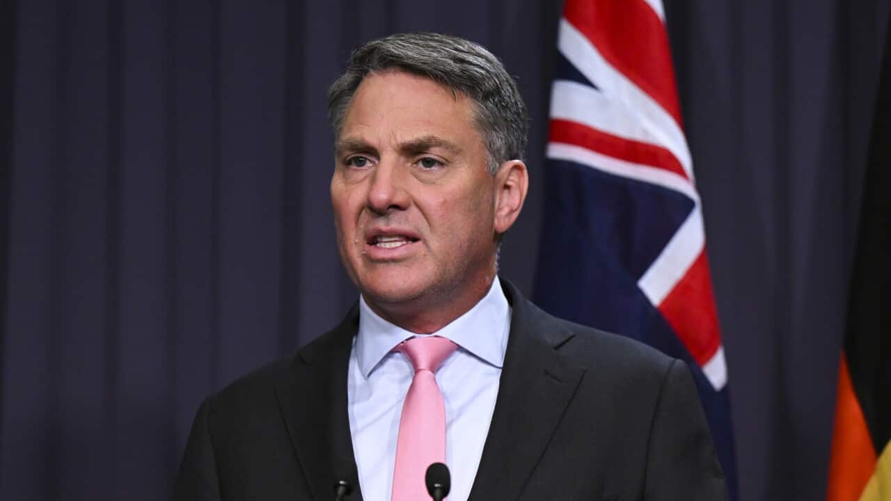 A man speaking into microphones while standing at a podium.