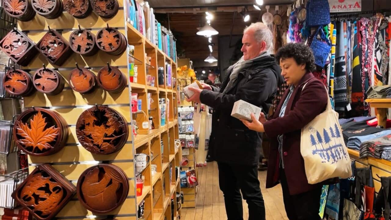 A man in a black winter coat and a woman in a burgundy coat are looking at items at a souvenir shop 